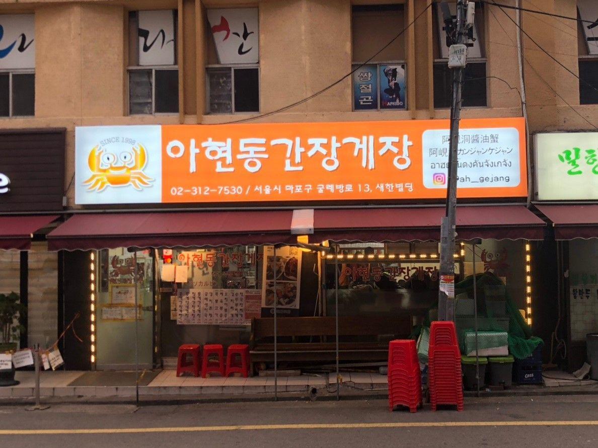 แม่นี่คือด้านหน้าของร้านอาหาร Ahyundong Ganjang Gejang ในกรุงโซล ที่โดดเด่นด้วยป้ายไม้และเก้าอี้สีแดงหน้าร้าน